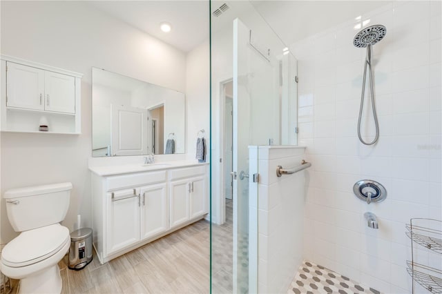 full bath with toilet, wood finished floors, visible vents, vanity, and a tile shower