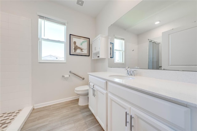 full bathroom with toilet, vanity, visible vents, baseboards, and tiled shower