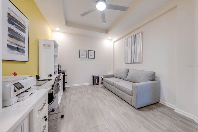 home office with light wood-style flooring, baseboards, ceiling fan, and a tray ceiling