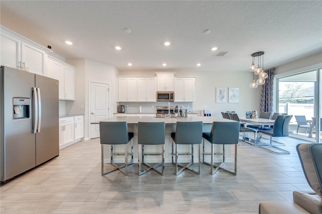 kitchen featuring visible vents, appliances with stainless steel finishes, a kitchen island with sink, and white cabinets