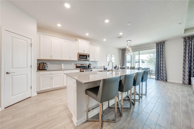 kitchen featuring a sink, white cabinets, appliances with stainless steel finishes, a kitchen bar, and a center island with sink