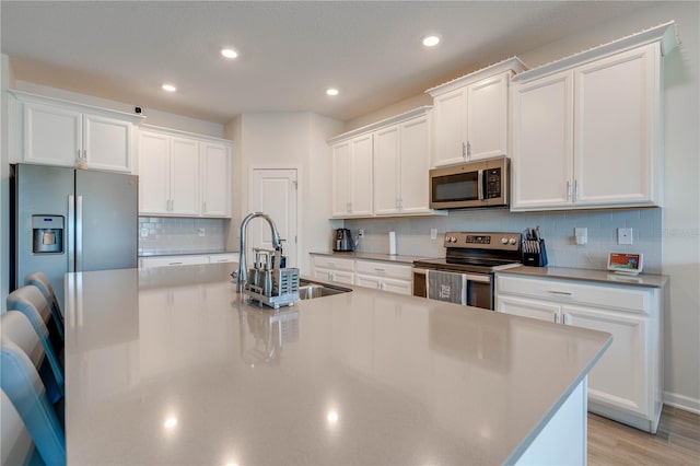 kitchen with a spacious island, a sink, white cabinetry, appliances with stainless steel finishes, and backsplash