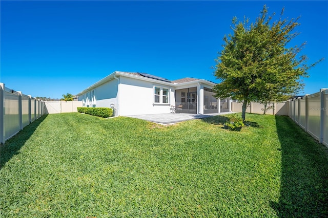 rear view of property with a sunroom, a fenced backyard, a lawn, and solar panels