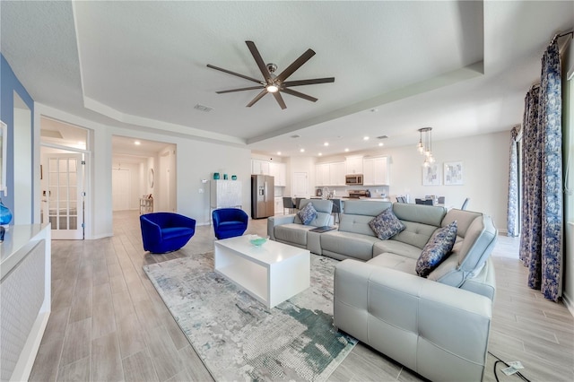 living room with visible vents, ceiling fan, a raised ceiling, and light wood-style flooring