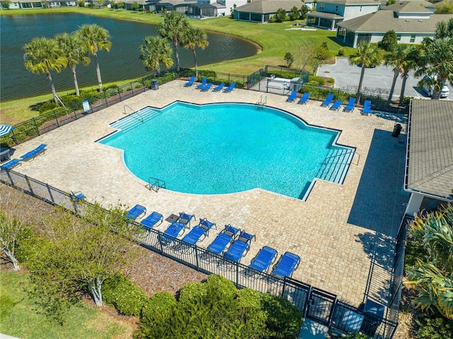 pool with a water view, a patio area, fence, and a yard