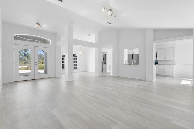 unfurnished living room featuring light wood-style floors, french doors, high vaulted ceiling, and baseboards