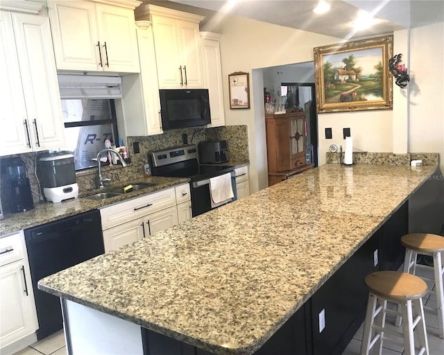 kitchen featuring a peninsula, a breakfast bar, a sink, backsplash, and black appliances