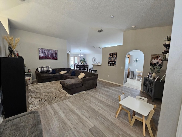 living area featuring visible vents, arched walkways, wood finished floors, an inviting chandelier, and a textured ceiling