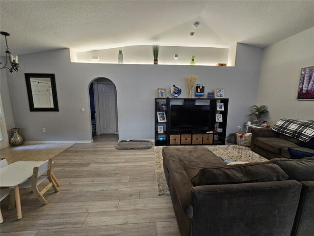 living area with light wood-style floors, arched walkways, vaulted ceiling, and a textured ceiling