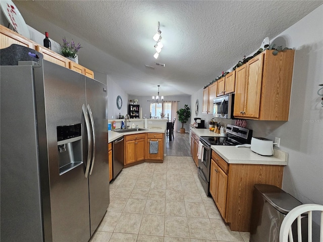 kitchen with light countertops, appliances with stainless steel finishes, a sink, a chandelier, and a peninsula