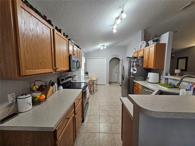 kitchen featuring light tile patterned floors, arched walkways, lofted ceiling, stainless steel appliances, and a sink