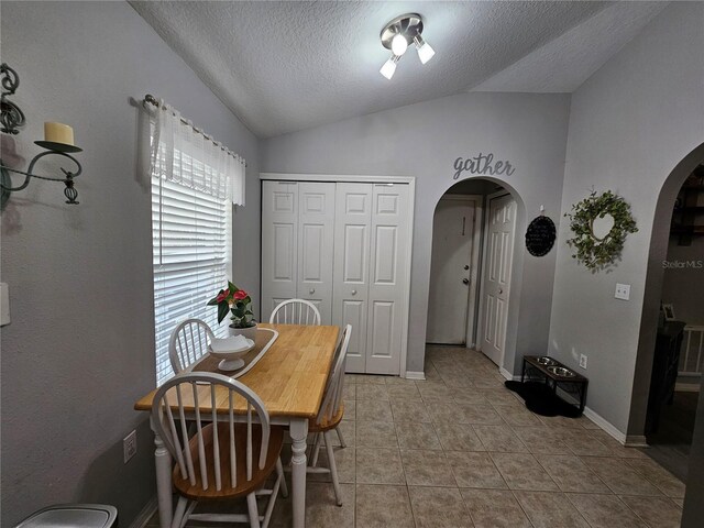 dining space featuring arched walkways, light tile patterned floors, a textured ceiling, lofted ceiling, and baseboards