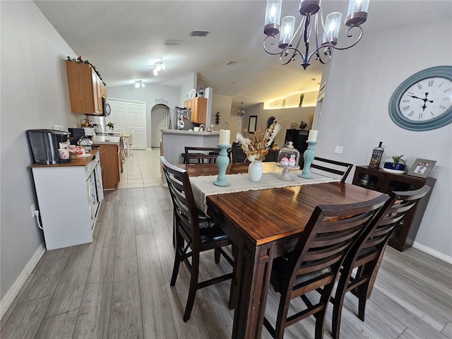 dining room with light wood finished floors, visible vents, arched walkways, baseboards, and vaulted ceiling