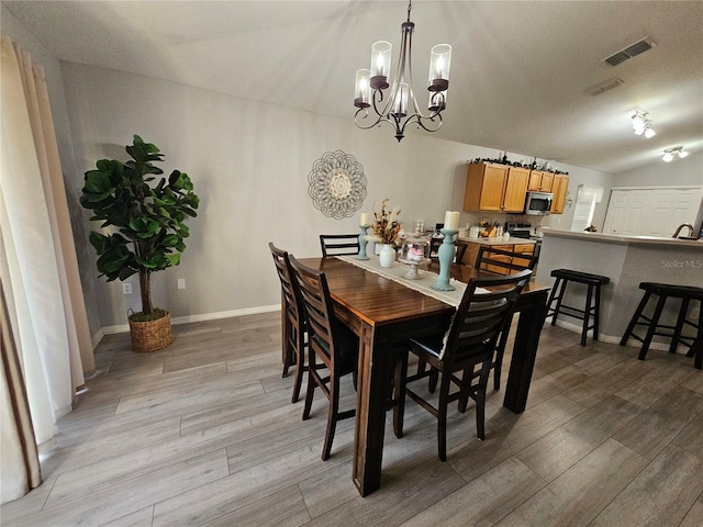 dining area with light wood-type flooring, baseboards, visible vents, and vaulted ceiling