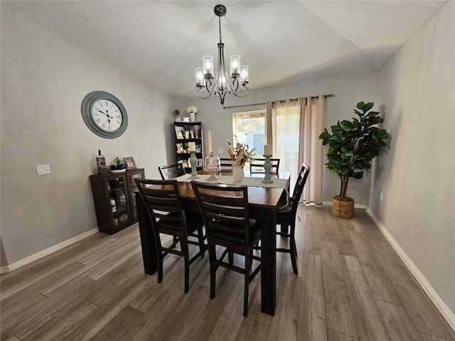 dining space featuring an inviting chandelier, a textured ceiling, baseboards, and wood finished floors