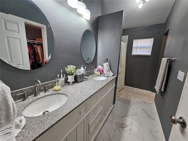 bathroom with marble finish floor, a textured ceiling, baseboards, and a sink