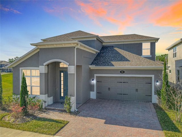 view of front facade with a shingled roof, decorative driveway, an attached garage, and stucco siding