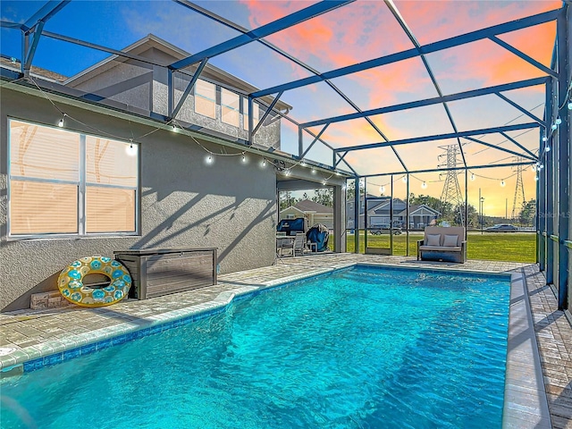 pool at dusk with an outdoor pool, a patio, a lanai, and a lawn