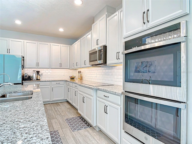 kitchen with appliances with stainless steel finishes, wood tiled floor, a sink, and decorative backsplash