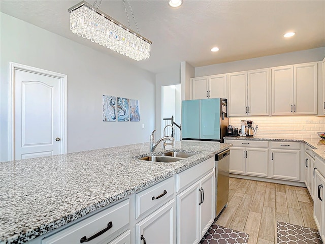 kitchen with light stone counters, backsplash, a sink, white cabinetry, and stainless steel dishwasher