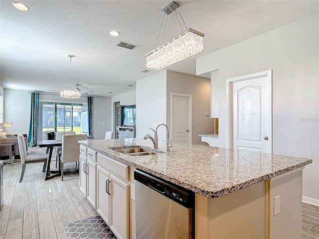 kitchen with an island with sink, an inviting chandelier, wood finish floors, stainless steel dishwasher, and a sink