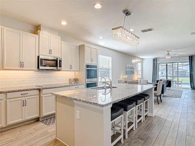 kitchen with stainless steel appliances, tasteful backsplash, visible vents, wood tiled floor, and a sink