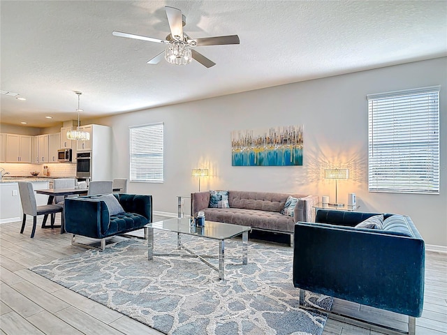 living room featuring wood finish floors, ceiling fan, a textured ceiling, and baseboards