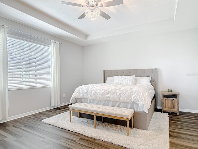 bedroom with a ceiling fan, a raised ceiling, baseboards, and wood finished floors