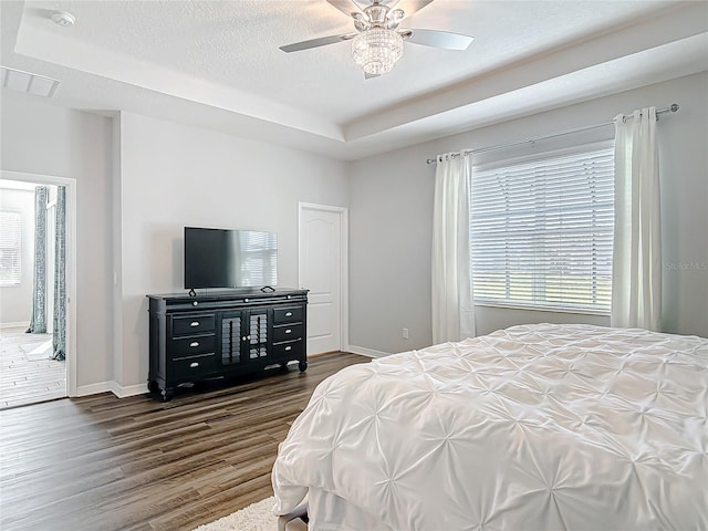 bedroom featuring a tray ceiling, dark wood finished floors, ceiling fan, a textured ceiling, and baseboards