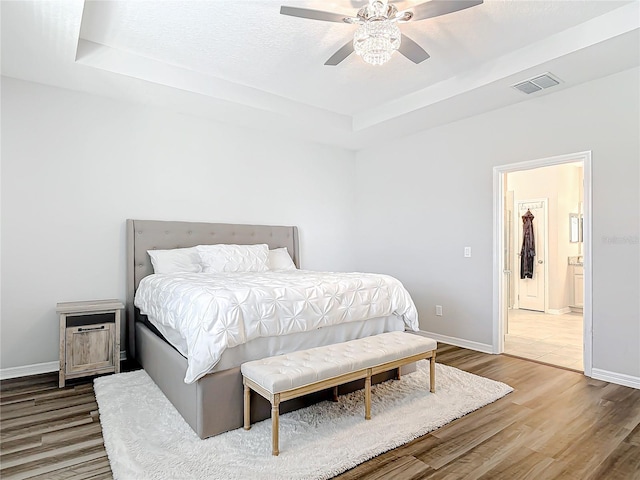 bedroom with a tray ceiling, wood finished floors, visible vents, and baseboards