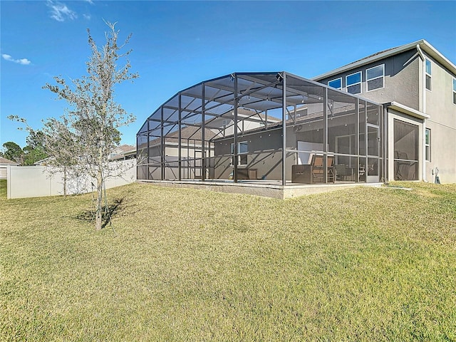 back of house featuring a lanai, fence, a lawn, and stucco siding