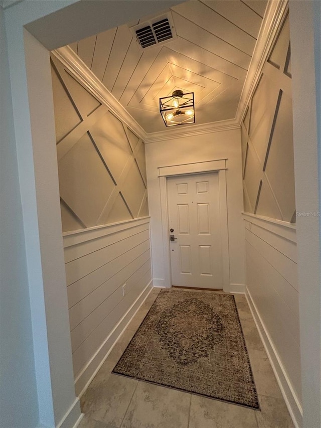 entryway with a decorative wall, visible vents, and crown molding