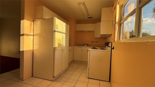 kitchen with light tile patterned flooring, white appliances, a sink, white cabinets, and light countertops