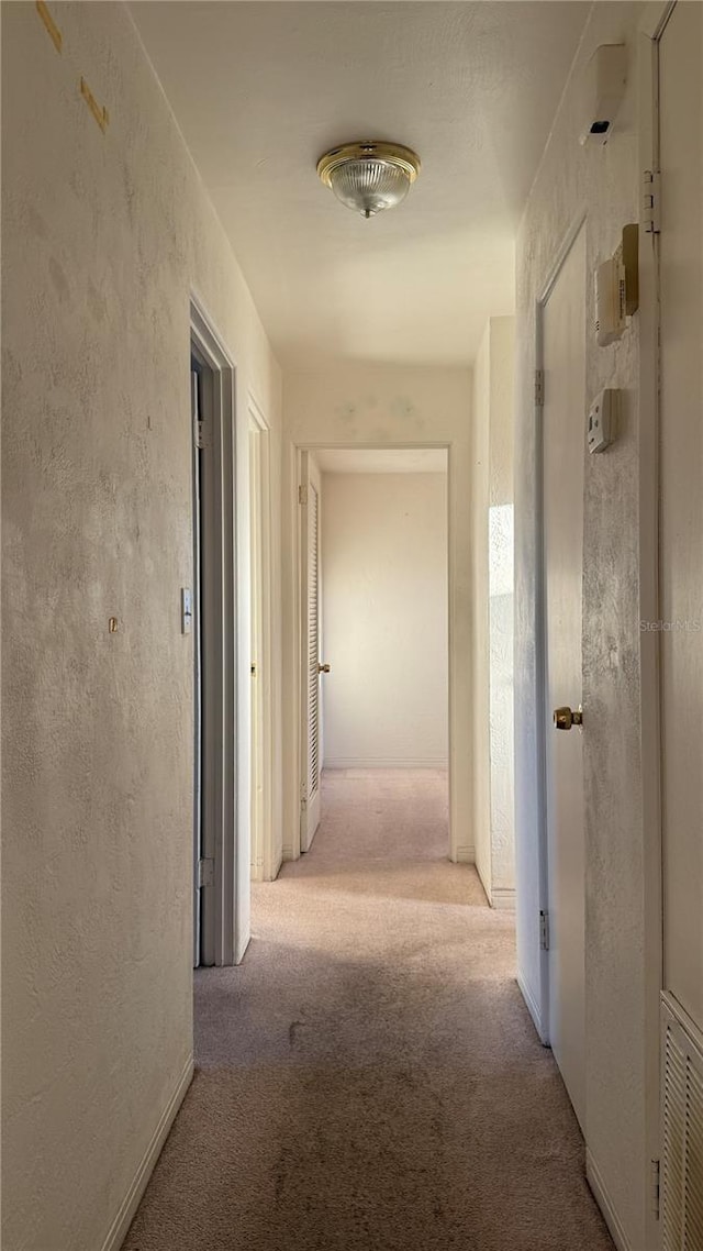 corridor with visible vents, carpet flooring, and a textured wall