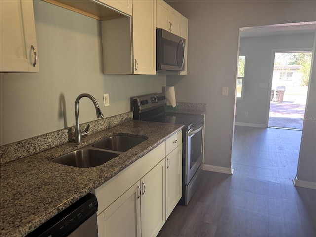 kitchen featuring appliances with stainless steel finishes, white cabinetry, a sink, dark stone countertops, and baseboards