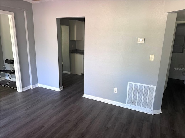 unfurnished room with baseboards, visible vents, and dark wood-style flooring