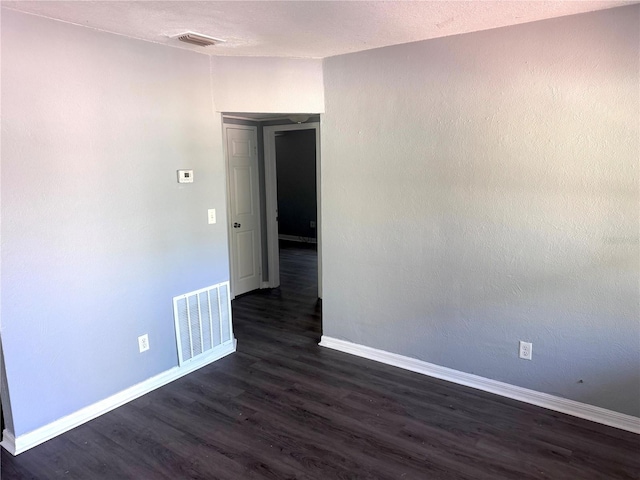 empty room with dark wood-style floors, visible vents, and baseboards