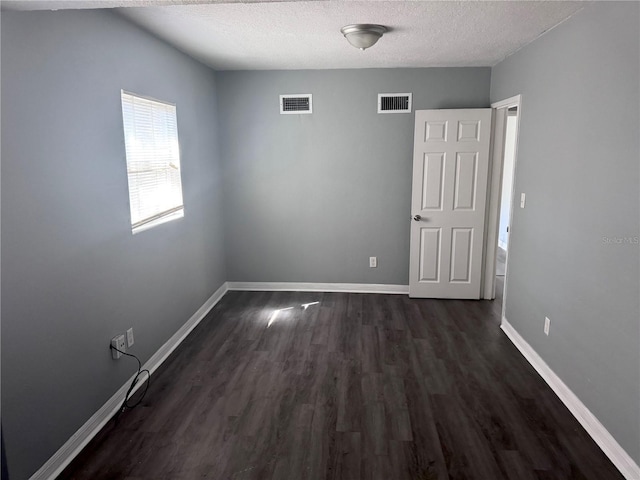 unfurnished room featuring baseboards, visible vents, dark wood finished floors, and a textured ceiling