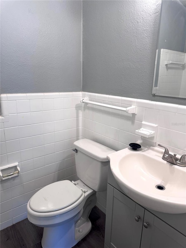 bathroom featuring wainscoting, toilet, wood finished floors, vanity, and tile walls