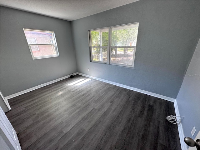 empty room with plenty of natural light, dark wood finished floors, and baseboards