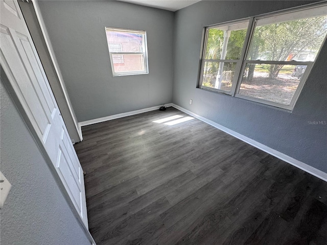 unfurnished room featuring a textured wall, dark wood-type flooring, and baseboards