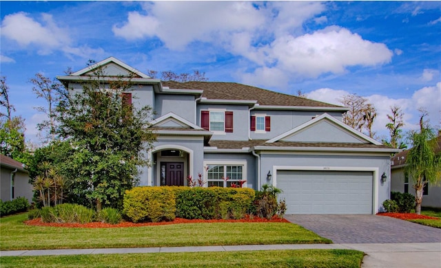 traditional-style house with a garage, a front lawn, decorative driveway, and stucco siding