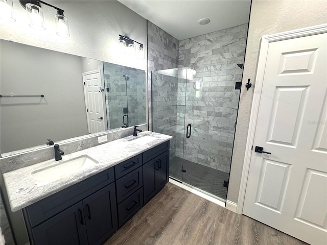 bathroom with double vanity, wood finished floors, a stall shower, and a sink