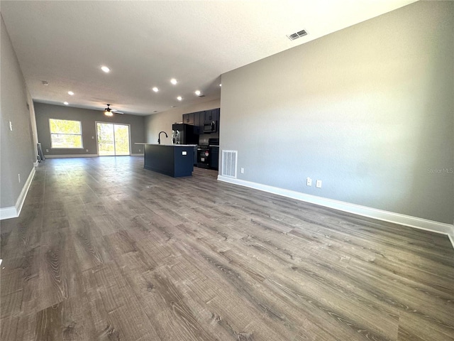 unfurnished living room featuring visible vents, dark wood-type flooring, baseboards, and a sink