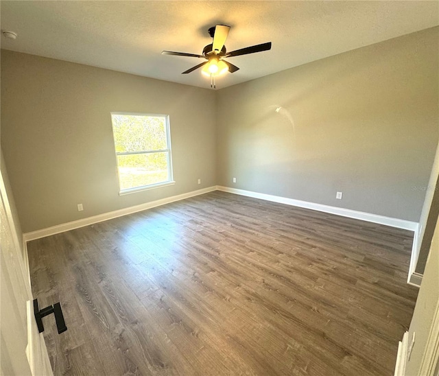 empty room with a textured ceiling, a ceiling fan, baseboards, and dark wood-style flooring