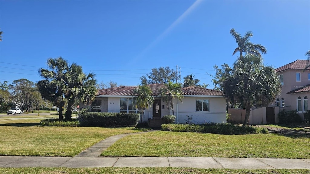 view of front of home featuring a tile roof, fence, a front lawn, and stucco siding