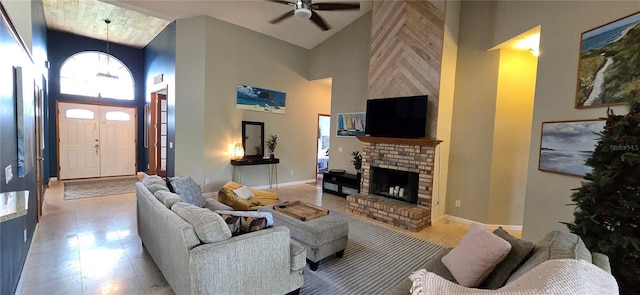 living room with a ceiling fan, a brick fireplace, a towering ceiling, and baseboards