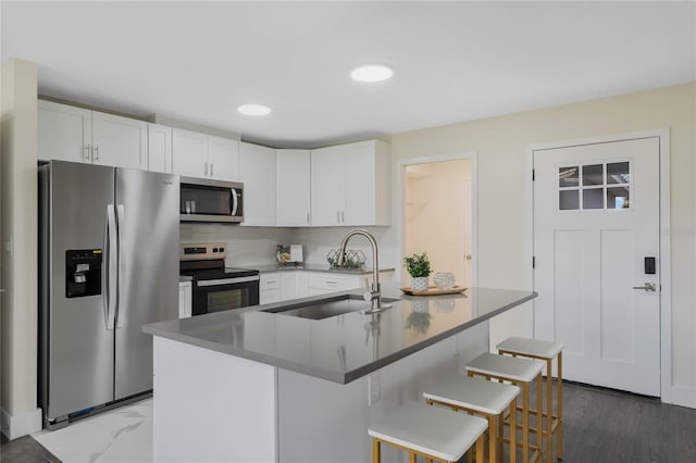 kitchen featuring appliances with stainless steel finishes, a sink, white cabinetry, and a kitchen breakfast bar