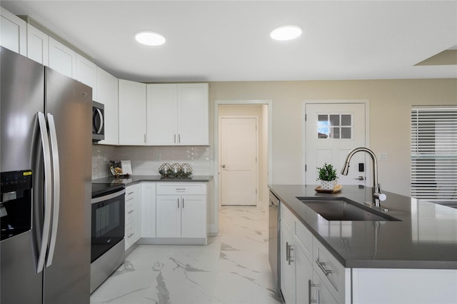 kitchen with dark countertops, a sink, marble finish floor, stainless steel appliances, and backsplash