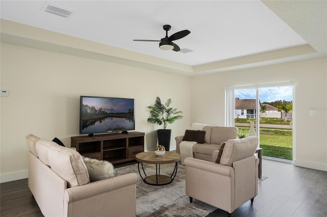 living area featuring baseboards, visible vents, ceiling fan, wood finished floors, and a tray ceiling